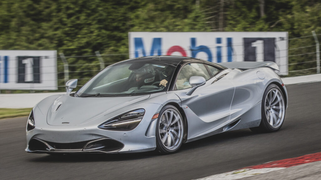 A silver mclaren driving down the road near trees.